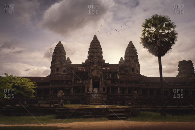 Stone oriental temple with shabby facade and towers on background of majestic sunset sky in Cambodia