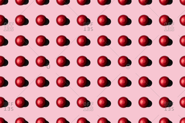 Top view of red coffee pods placed in even rows as seamless pattern on pink background