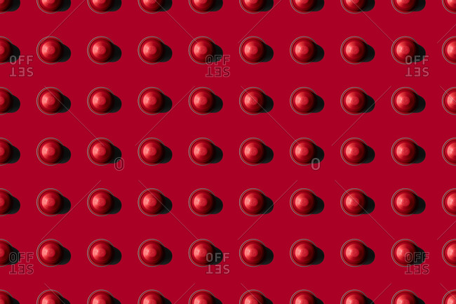 Top view of red coffee pods placed in even rows as seamless pattern on red background