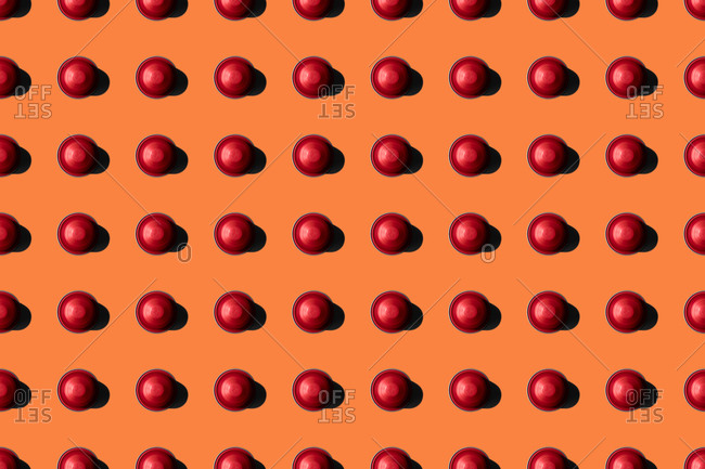 Top view of red coffee pods placed in even rows as seamless pattern on orange background