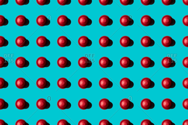 Top view of red coffee pods placed in even rows as seamless pattern on blue background