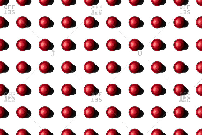 Top view of red coffee pods placed in even rows as seamless pattern on white background