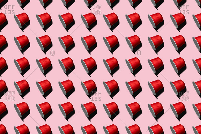 Top view of red coffee pods placed in even rows as seamless pattern on pink background