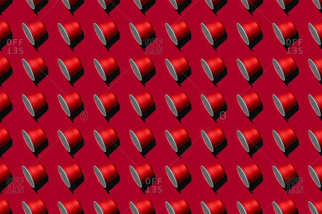 Top view of red coffee pods placed in even rows as seamless pattern on red background