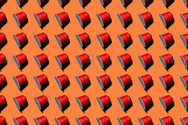Top view of red coffee pods placed in even rows as seamless pattern on orange background