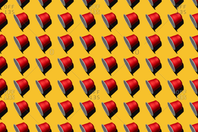 Top view of red coffee pods placed in even rows as seamless pattern on yellow background
