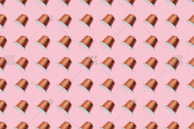 Top view of golden coffee pods placed in even rows as seamless pattern on pink background