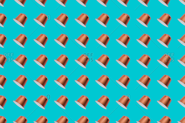 Top view of golden coffee pods placed in even rows as seamless pattern on blue background