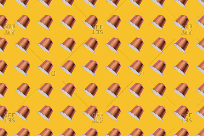 Top view of golden coffee pods placed in even rows as seamless pattern on yellow background