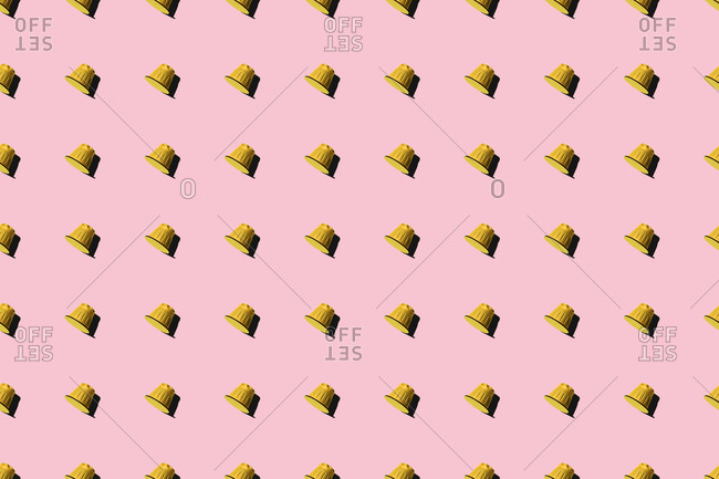 Top view of yellow coffee pods placed in even rows as seamless pattern on pink background