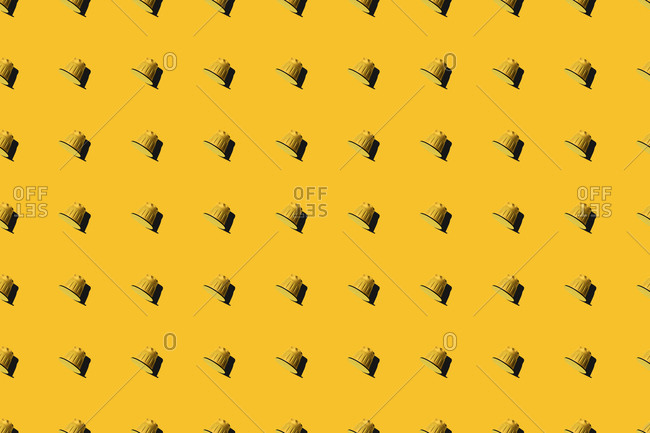 Top view of yellow coffee pods placed in even rows as seamless pattern on yellow background
