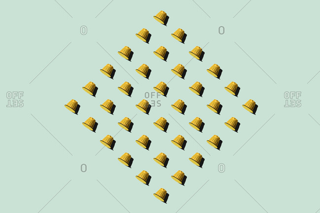 Top view of yellow coffee pods placed in even rows as seamless pattern on green background