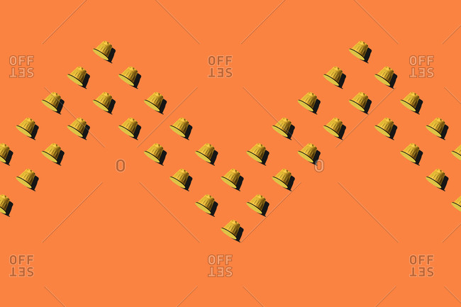 Top view of yellow coffee pods placed in even rows as seamless pattern on orange background