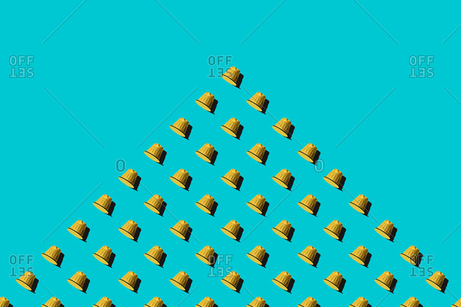 Top view of yellow coffee pods placed in even rows as seamless pattern on blue background