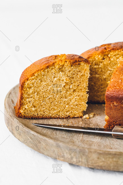 Delicious sweet sliced sponge cake placed with knife on wooden board against white background