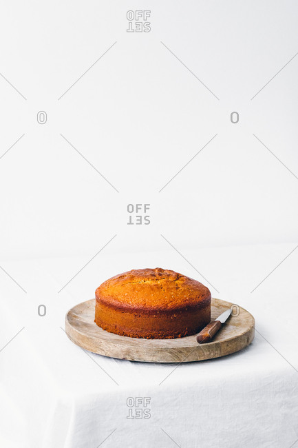 Delicious sweet sliced sponge cake placed with knife on wooden board against white background