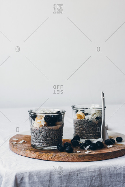 Glass jars with delicious chia puddings made of fresh tasty almond milk and chia seeds with honey topped with blackberries and sliced banana served on wooden board against white background