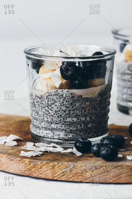 Glass jars with delicious chia puddings made of fresh tasty almond milk and chia seeds with honey topped with blackberries and sliced banana served on wooden board against white background