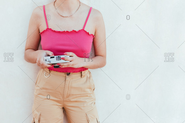 Cropped unrecognizable female taking pictures on vintage photo camera on a white wall background