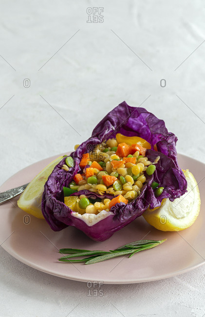 From above of colorful purple cabbage leaf filled with mix of peppers and lentils near slice of fresh lemon and Himalayan salt on dark plates