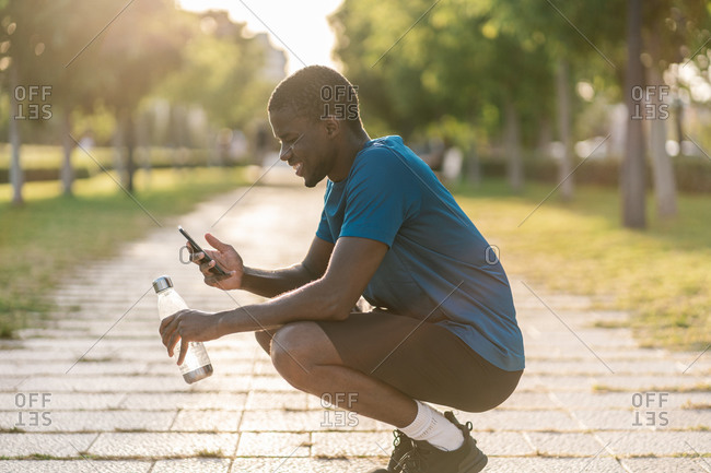 African black man in sports clothes sitting down and taking selfie in the park
