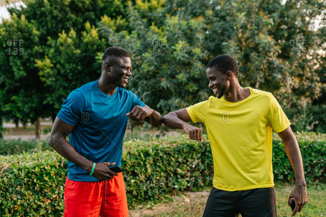 Two black men in colorful sport clothes greeting doing the elbow bump outdoors in the park
