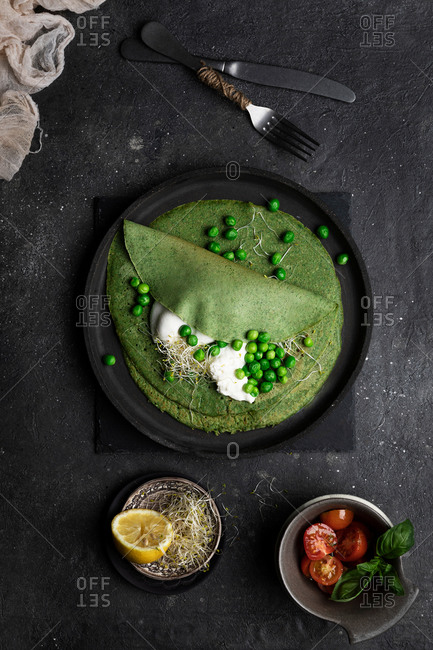 Overhead still life of pea crepes served on a dark dish placed on dark textured board