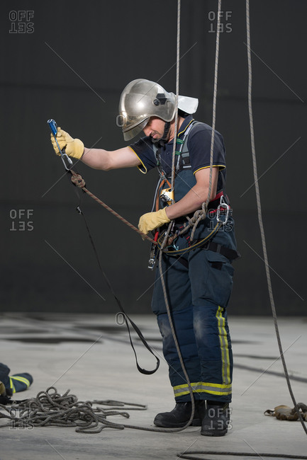 Determined fireman wearing protective uniform and hardhat adjusting ropes before practice