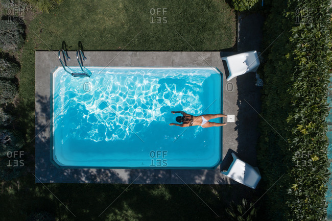 From above drone view of relaxed young female getting inside the water in pool and enjoying summer vacation while spending time in green yard