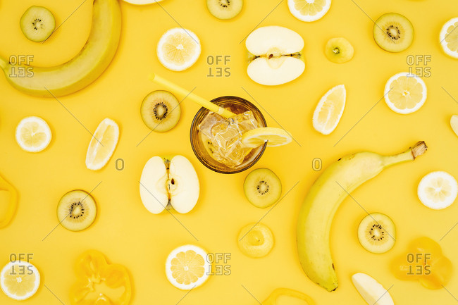 Top view of various fresh fruits and vegetables arranged on yellow background with glass of cocktail with straw and ice