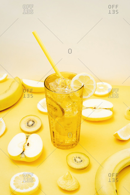 Various fresh fruits and vegetables arranged on yellow background with glass of cocktail with straw and ice