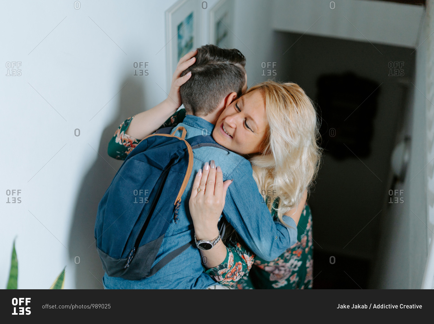 Content mother gently kissing teenage son with school backpack while hugging together on steps in cozy modern house