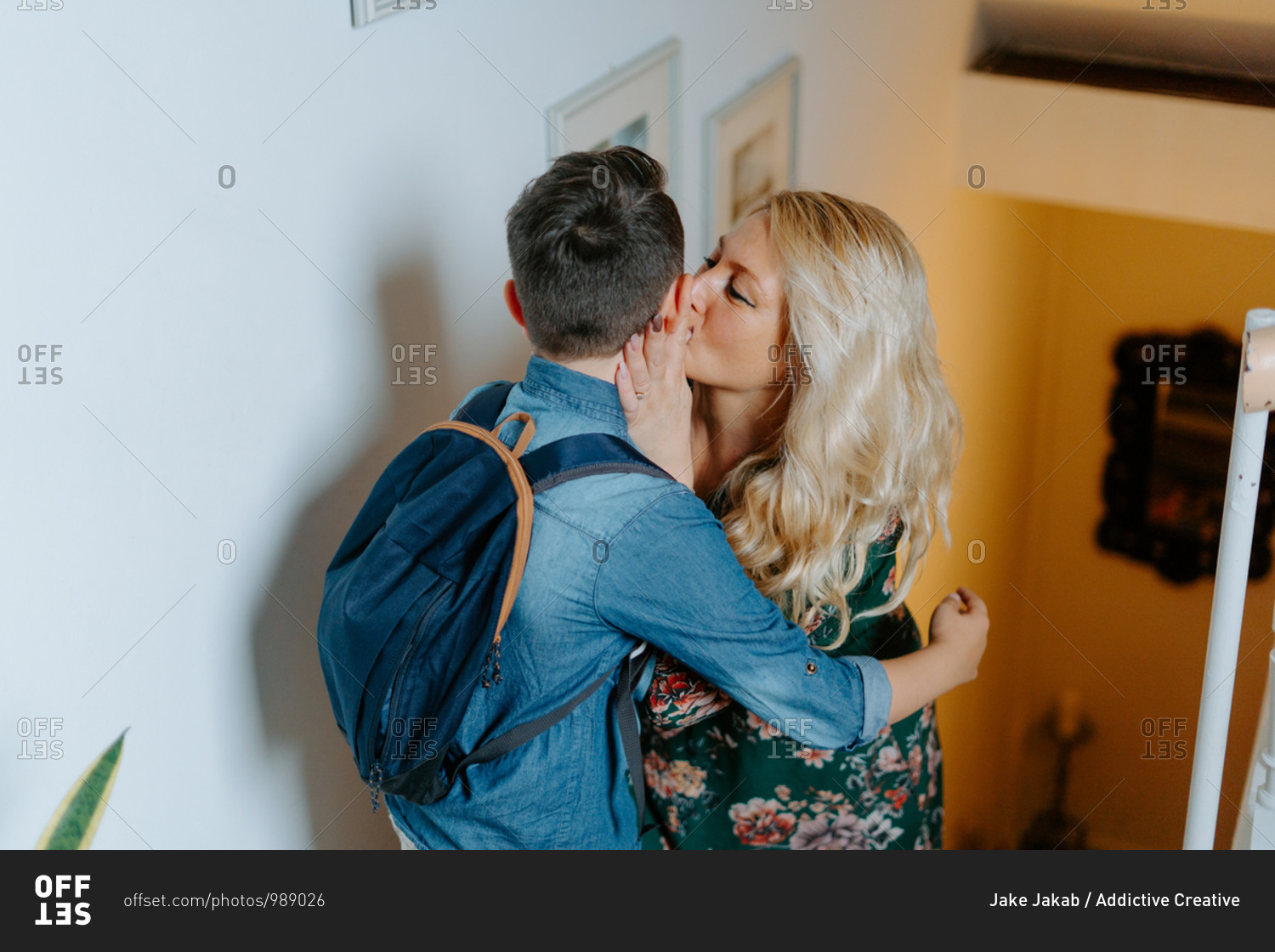 Content mother gently kissing teenage son with school backpack while hugging together on steps in cozy modern house