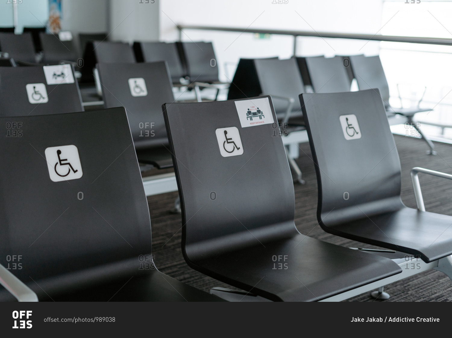 Rows of empty black seats in public waiting area for people with physical disabilities and people with special needs with square white sign demonstrating person on wheelchair