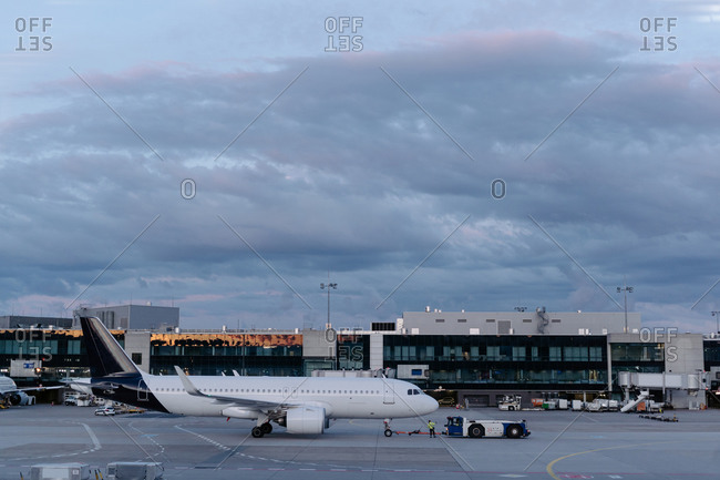 Contemporary white aircraft parked on airfield near modern glass airport terminal against picturesque cloudy dark blue sky