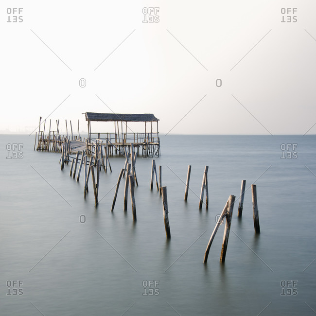 Abandoned partially destroyed dock made of thick wooden sticks on endless ocean with pure water under serene sky in daylight