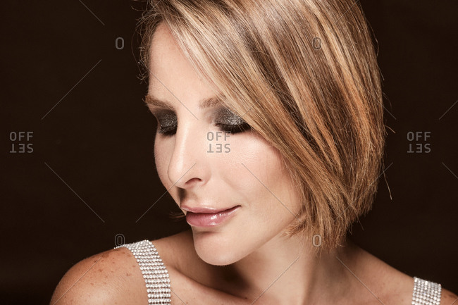 Close up portrait of a sexy blonde woman wearing a shiny grey top looking down on a black background