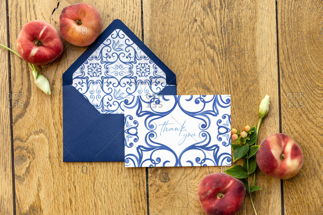 From above ripe peaches and delicate flowers placed on lumber table near envelope with elegant greeting card