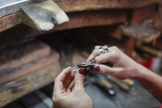 From above anonymous female artisan using pliers to create silver accessory over workbench during work in studio