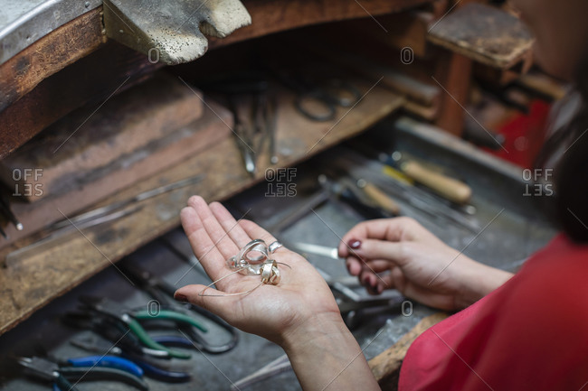 From above anonymous craftswoman demonstrating bunch of silver accessories over workbench in workshop