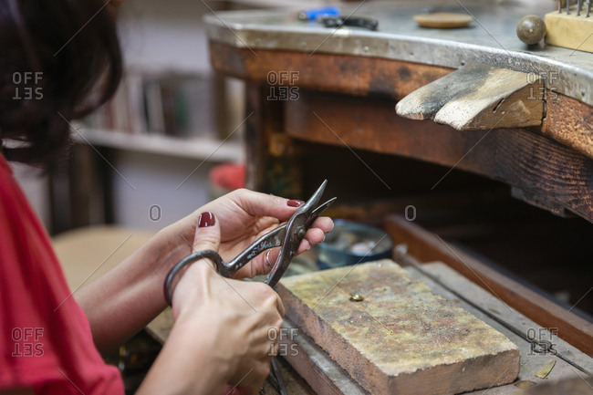 Crop female jeweler cutting silver over workbench while creating accessories in professional workbench