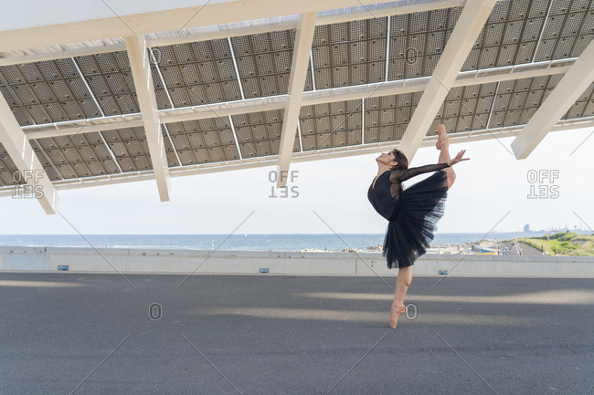 Side view of a young race female ballet dancer wearing a black tutu standing in a ballet pose with leg raised abroad