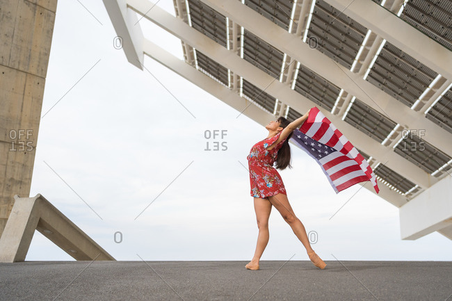 Young ballerina dancing while holding USA national flag outdoors