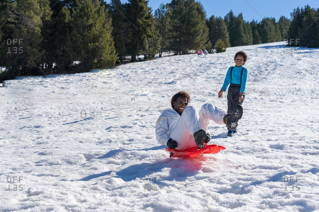 Black woman dressed in a white jumpsuit has fun with a sled under the eyes of her son