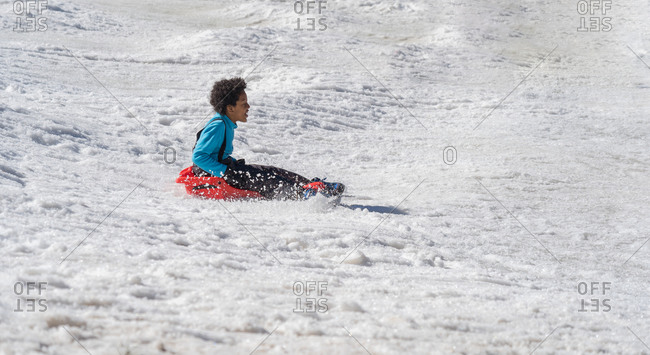 Happy black boy sledding down from the snow slope