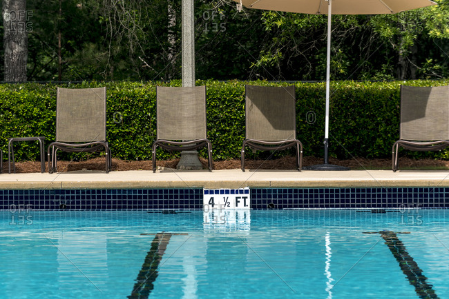 Swimming pool deck lounge chairs lined up by the side of a pool.