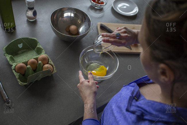Overhead view of a female separating eggs into a bowl.