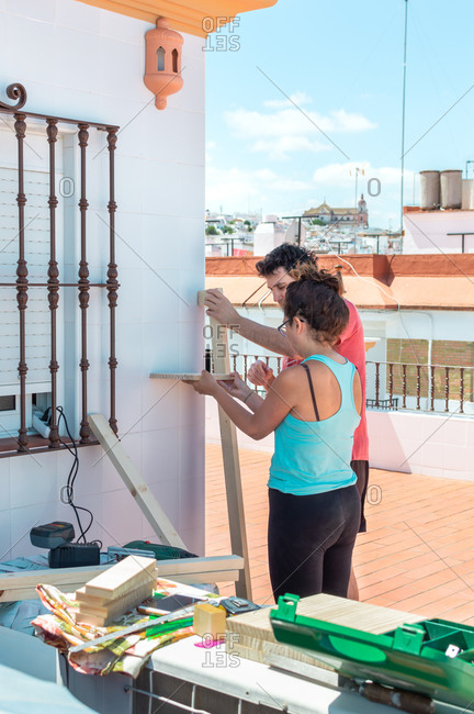 Couple working together to build a shelf on the rooftop of a house.