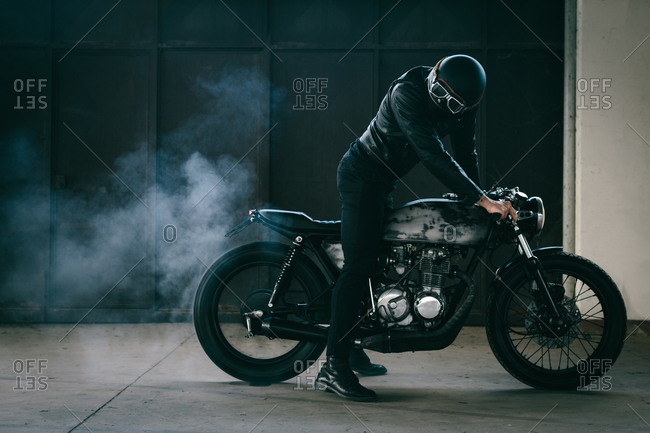 Young male motorcyclist revving vintage motorcycle in garage