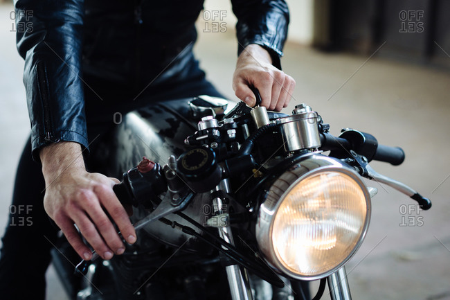 Young male motorcyclist straddling vintage motorcycle in garage, cropped